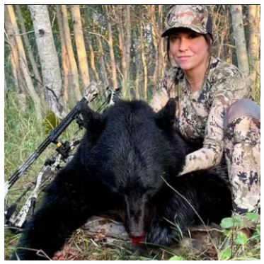Person in camouflage attire with a hunted bear in a forest setting