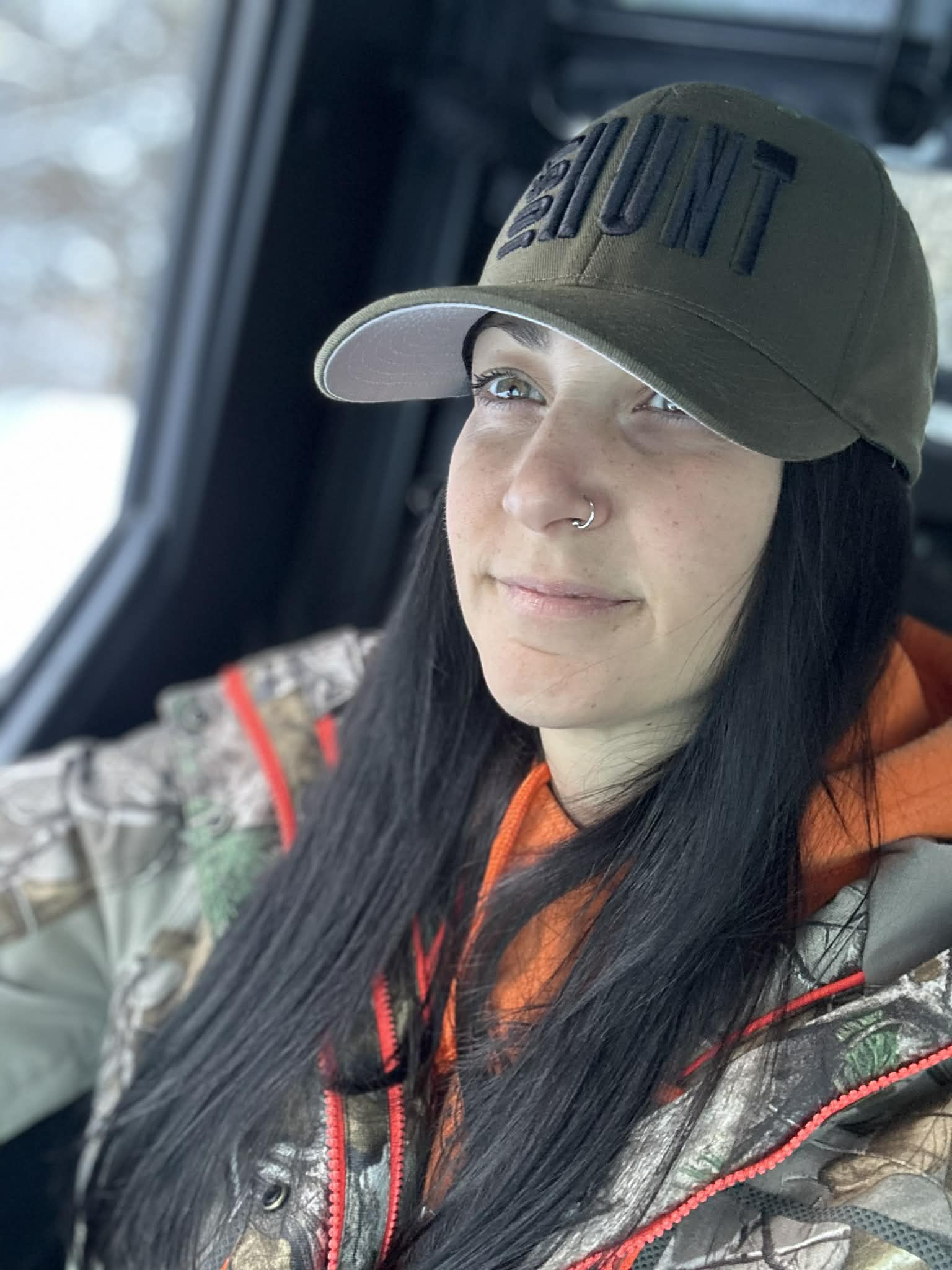 Woman wearing a cap with 'The Hunt' text, sitting inside a vehicle.