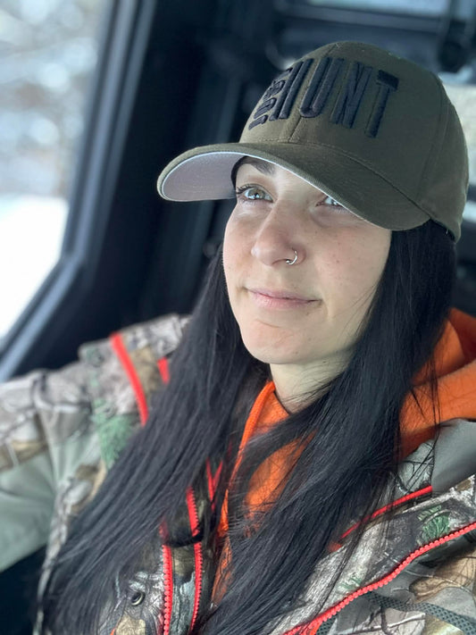 Woman wearing a cap with 'The Hunt' text, sitting inside a vehicle.